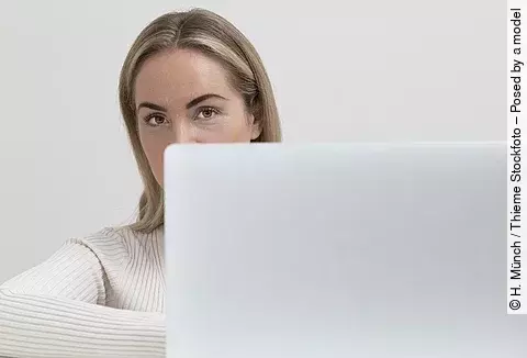 Frau mit blonden Haaren, die hinter einem Laptop hervorschaut.
