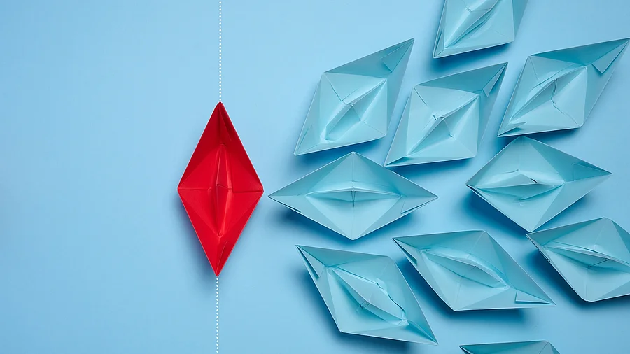 Symbolbild Resilienz rotes Papierboot umzingelt von vielen blauen