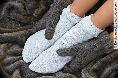 Hände in Handschuhen greifen um Füße in dicken Socken.