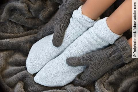 Hände in Handschuhen greifen um Füße in dicken Socken.