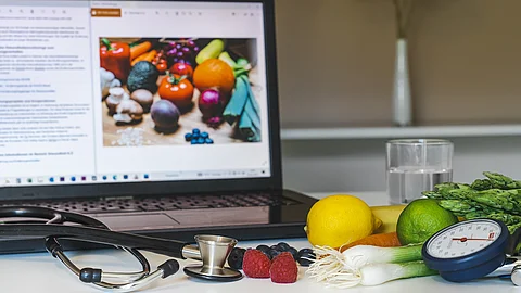 Bildschirm, Stethoskop und gesunde Lebensmittel wie Gemüse auf einem Schreibtisch