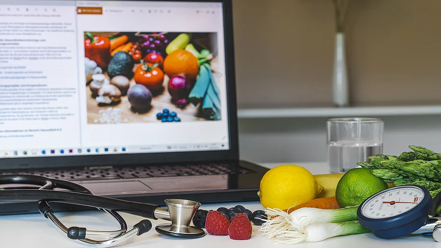 Bildschirm, Stethoskop und gesunde Lebensmittel wie Gemüse auf einem Schreibtisch