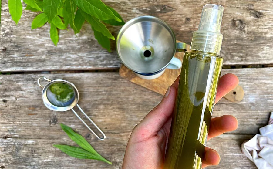 Frauenhand mit einer Flasche Sprühkopf über einem Holztisch gehalten. Die Flasche enthält eine grünliche Flüssigkeit