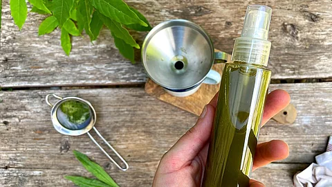 Frauenhand mit einer Flasche Sprühkopf über einem Holztisch gehalten. Die Flasche enthält eine grünliche Flüssigkeit