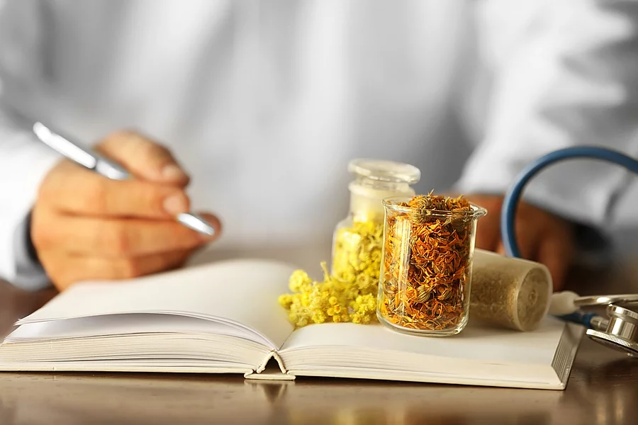 Männlicher Arzt mit Medizinbuch und Phytotherapeutika auf dem Tisch