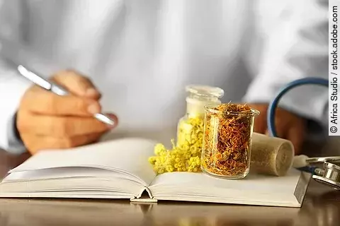 Männlicher Arzt mit Medizinbuch und Phytotherapeutika auf dem Tisch