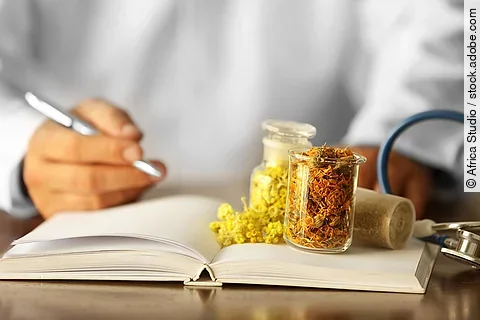 Männlicher Arzt mit Medizinbuch und Phytotherapeutika auf dem Tisch
