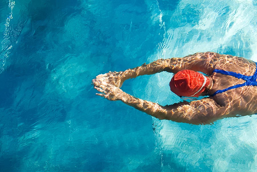 Frau mit roter Badekappe schwimmt im Schwimmbecken.