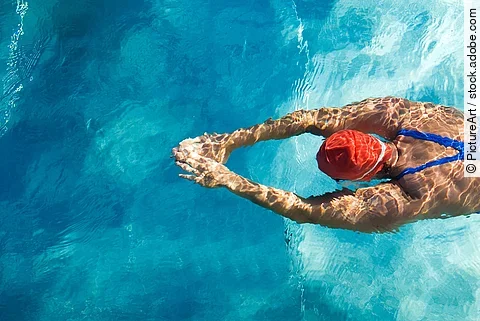 Frau mit roter Badekappe schwimmt im Schwimmbecken.