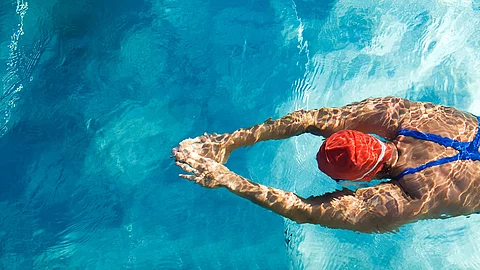 Frau mit roter Badekappe schwimmt im Schwimmbecken.