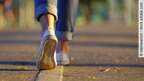Frauenbeine in Sneakern und Jeans laufen auf der Straße