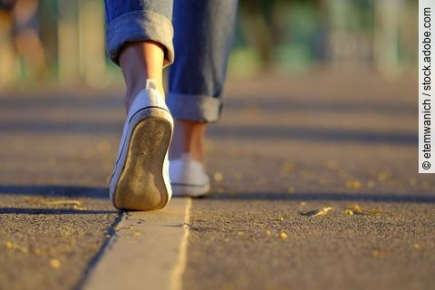 Frauenbeine in Sneakern und Jeans laufen auf der Straße