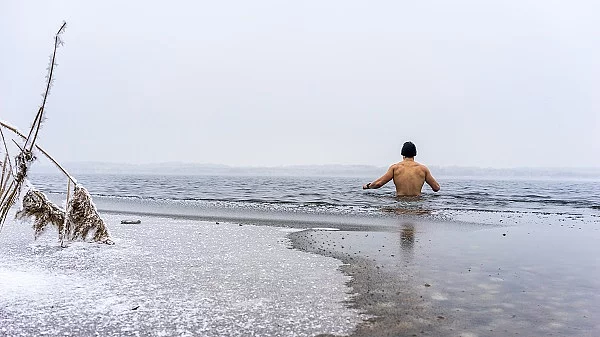 Junger Mann mit Mütze geht Eisbaden.
