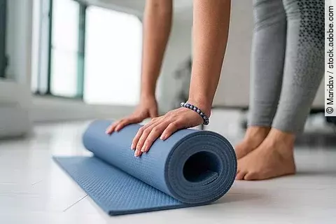 Frau rollt ihre Yogamatte zusammen.