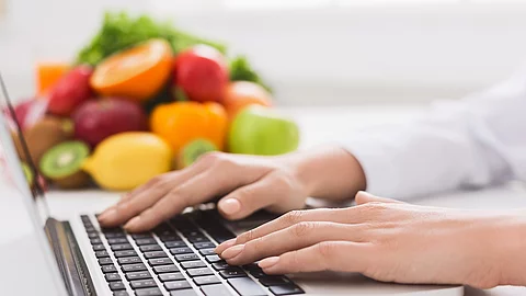 Ernährungsberaterin tippt auf Tastatur, daneben liegen Obst und Gemüse
