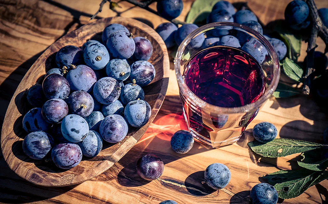 Schlehenfrüchten auf einem Tisch in einer Holzschale, daneben ein Glas mit rotem Likör.