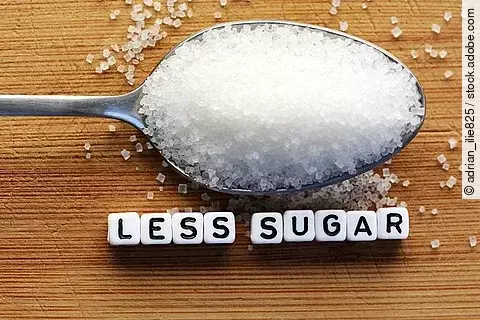 Zucker auf einem Esslöffel mit der Unterschrift Less Sugar.