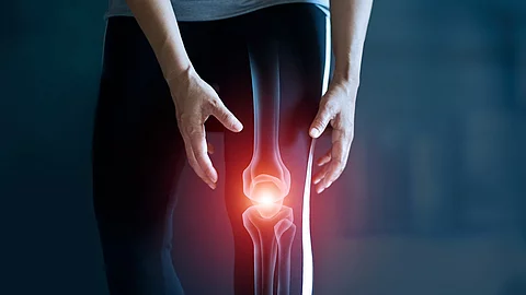 Frau hält sich das Knie, Kniegelenk ist rot illustriert als Symbol für Knieschmerz