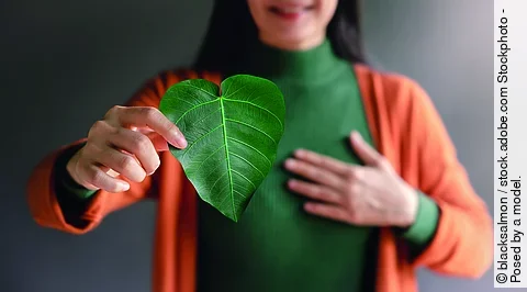Frau lächelt und hält ein Blatt in Herzform in die Kamera.