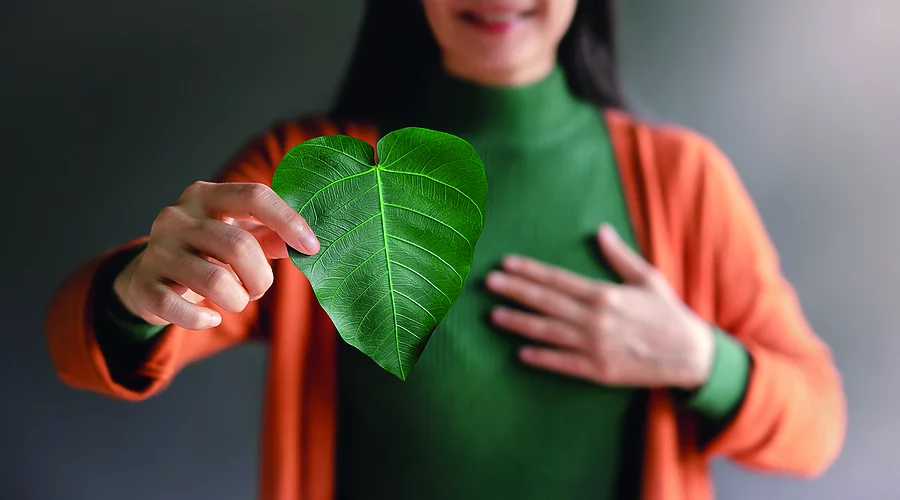 Frau lächelt und hält ein Blatt in Herzform in die Kamera.