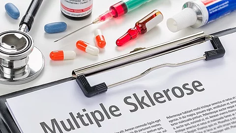 Klemmbrett mit einem Informationsblatt zu Multipler Sklerose. Darüber liegen Medikamente, Spritzen und ein Stethoskop. 