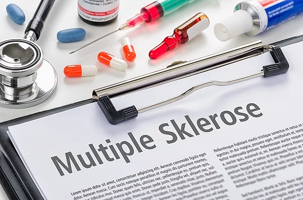 Klemmbrett mit einem Informationsblatt zu Multipler Sklerose. Darüber liegen Medikamente, Spritzen und ein Stethoskop. 