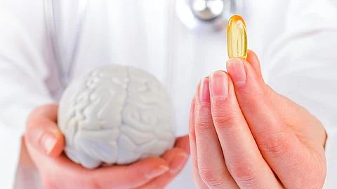 Frau hält ein Gehirnmodell in der linken Hand, in der rechten eine Fischölkapsel