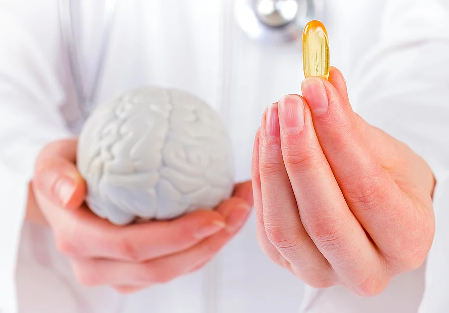 Frau hält ein Gehirnmodell in der linken Hand, in der rechten eine Fischölkapsel