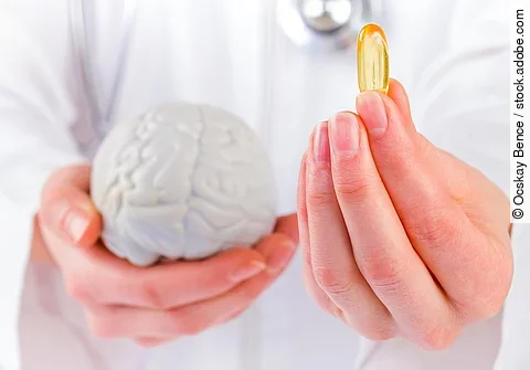 Frau hält ein Gehirnmodell in der linken Hand, in der rechten eine Fischölkapsel