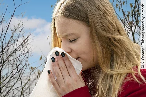 Frau niest ins Taschentuch, Heuschnupfenzeit, im Hintergrund Baumpollen