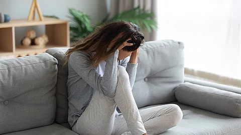 Junge Frau sitzt auf dem Sofa, die Hände halten den Kopf und bedecken das Gesicht.