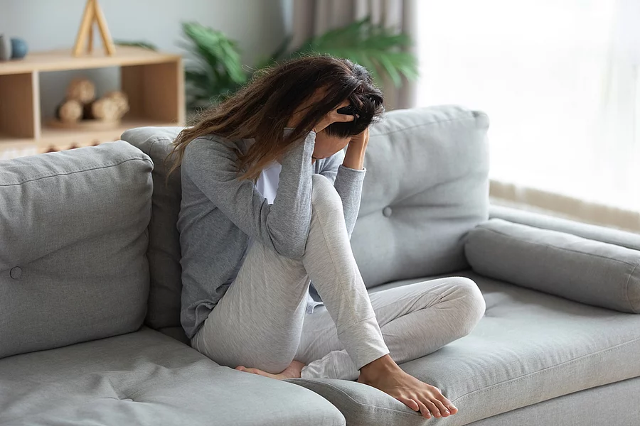 Junge Frau sitzt auf dem Sofa, die Hände halten den Kopf und bedecken das Gesicht.