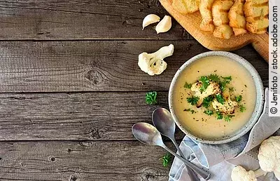Roasted cauliflower and potato and soup. Top view table scene. Side border over a rustic wood background with copy space. Blumenkohl-Kartoffel-Suppe auf Holzuntergrund