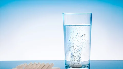 Wasserglas mit sprudelnder Tablette und Tabletten neben dem Glas Wasserglas mit sprudelnder Tablette und Tabletten