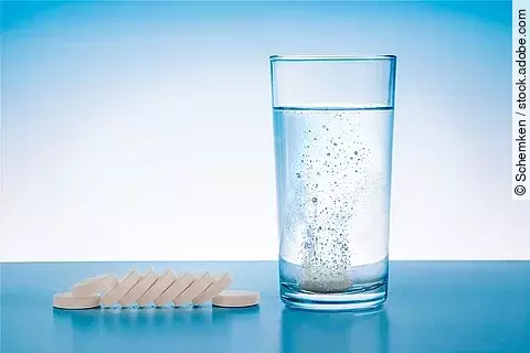 Wasserglas mit sprudelnder Tablette und Tabletten