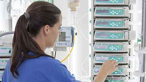 Junge Ärztin oder Krankenschwester stellt Perfusor am Patientenbett ein