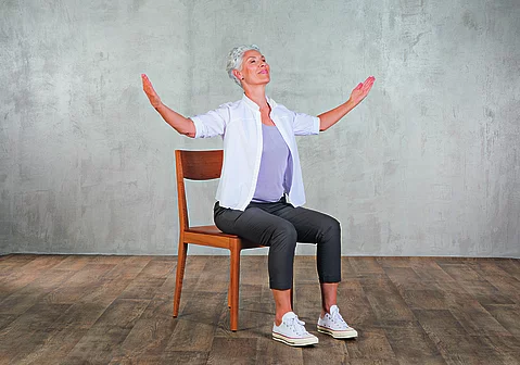 Frau im mittleren Alter praktiziert Yoga auf einem Stuhl aus Holz.