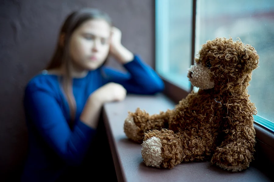 Child abuse at home Kind sitzt einsam an Fenster mit Teddybär