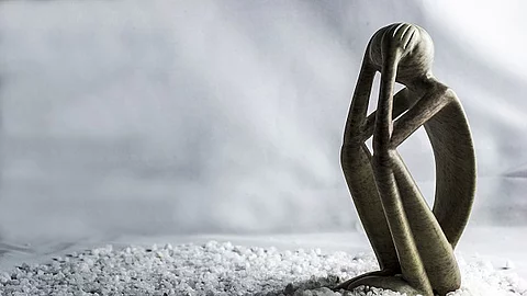 Gebeugt sitzende Holzfigur, traurig