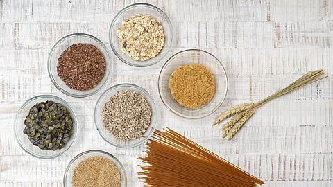 Vollkornprodukte: Nudeln, Grünkern, Leinsamen, Müsli, Kürbiskerne in Schüssln auf weißem Holzuntergrund