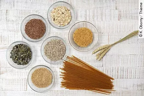 Vollkornprodukte: Nudeln, Grünkern, Leinsamen, Müsli, Kürbiskerne in Schüssln auf weißem Holzuntergrund