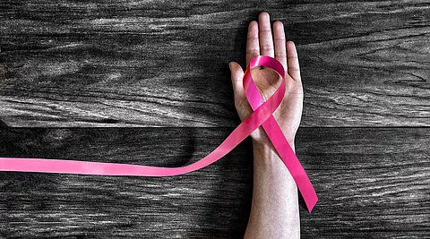 Hand mit Brustkrebsschleife auf dunklem Holzgrund