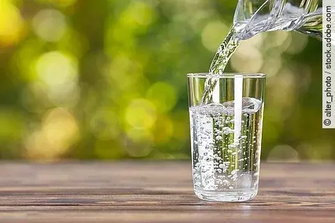 Wasser, das von einer Glaskaraffe in ein Glas geschüttet wird.