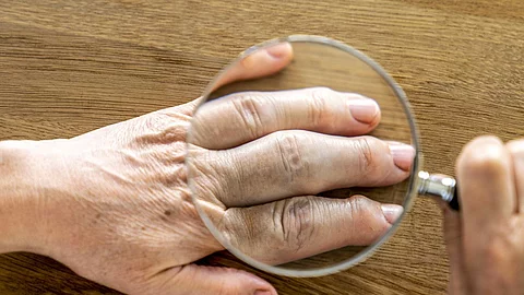 Hand die mit einer Lupe untersucht wird.
