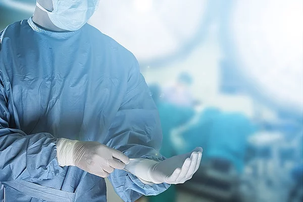 Medical team preparing equipment for surgery Operateurin zieht sich Handschuhe an