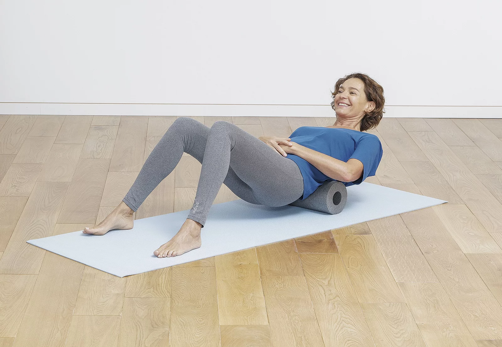 Eine Frau macht Übungen mit einer Faszienrolle auf eine Yogamatte.