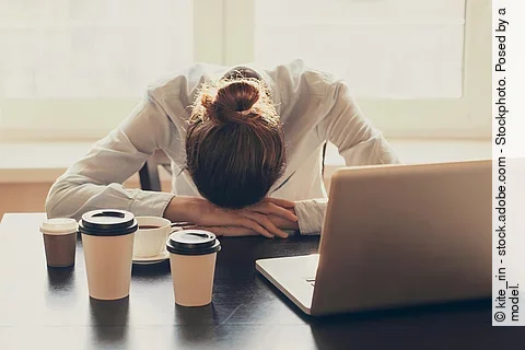 Businessfrau mit Kopf auf dem Schreibtisch, schlafend mit Kaffeebechern