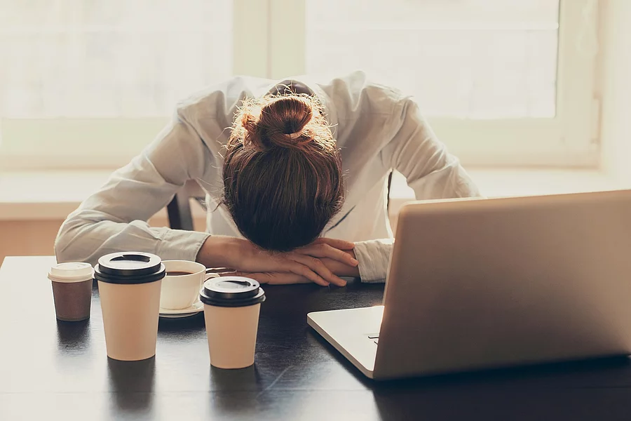 Businessfrau mit Kopf auf dem Schreibtisch, schlafend mit Kaffeebechern