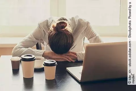 Businessfrau mit Kopf auf dem Schreibtisch, schlafend mit Kaffeebechern