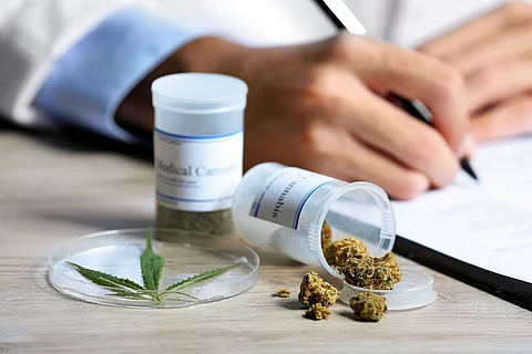Arzt füllt Rezept aus, daneben Behältnisse mit medizinischem Cannabis